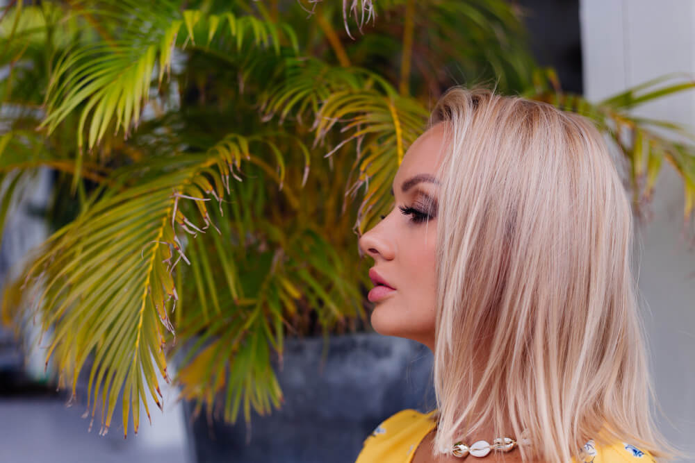 Blonde Frau mit Wimpernverlängerung im Sommer vor Palmen – Pflegetipps vom Glow Wow Studio München